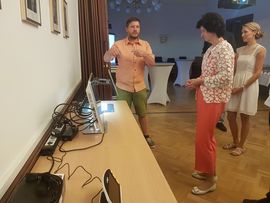 Frau steht vor Bildschirm ein Mann erkl&auml;rt ihr das Gesehene