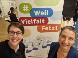 Mitarbeiterinnen des Inklusionsnetzwerk Sachsen Susanne R&ouml;&szlig;ner (links) und Heike Engelien (rechts) vor dem Roll-Up #WeilVielfaltfetzt am Stand des Inklusionsnetzwerk Sachsen
