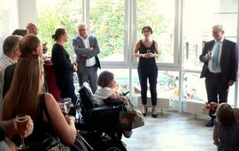 Menschen im Halbkreis als Zuh&ouml;rer und vorne eine Frau die eine Rede h&auml;lt