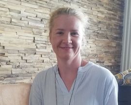 Freundlich l&auml;chelnde Frau mit blonden, zusammengebundenen Haaren, blickt in Kamera