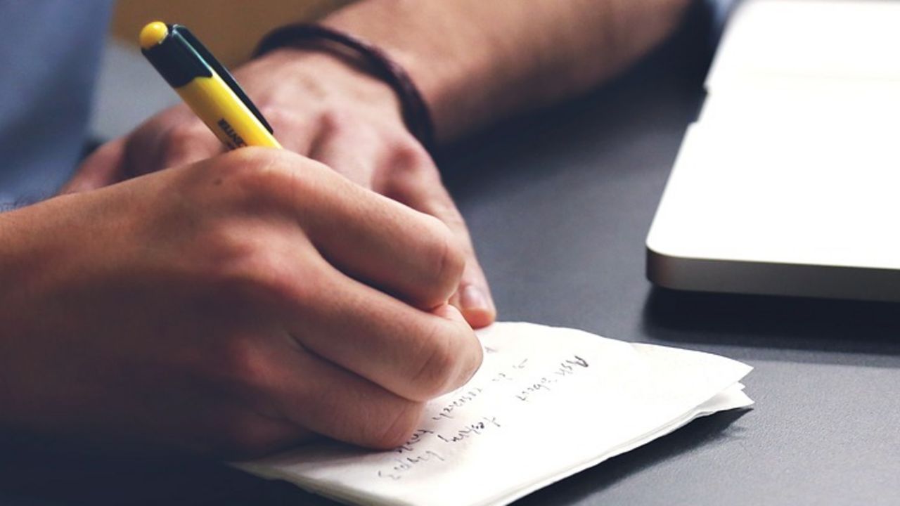 Männerhand sitzt am Laptop und macht Notizen