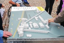 Ein Tastmodell des Bergbaumuseums. Es stehen Menschen um das Modell herum und drei H&auml;nde betasten es vorsichtig