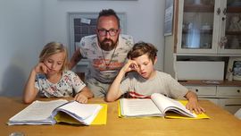 Vater mit zwei Kindenr am Tisch vor Schulb&uuml;chern und Heften