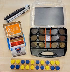 Auf einem Holztisch liegen verschiedene Arbeitsmaterialen der LAG SH Sachsen für die Schuleinsätze. Simulationsbrillen für Augenerkrankungen, Dumme Fragen Kartenset, ein Langstock und ein Hör-Memory-Spiel