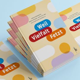 Ein Stapel des Buches "Weil Vielfalt fetzt". Zu sehen ist die Vorderseite des Buches. Auf dieser Vorderseite steht: "Herausgeberinnen - Marscha Richarz, Kaddu Cutz und LAG Selbsthilfe Sachsen e.V.". Darunter sieht man das Logo "Weil (blau) Vielfalt (rot) fetzt (orange)".