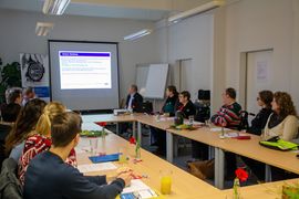 Teilnehmern sitzen in U-Form am Tisch und h&ouml;ren zu