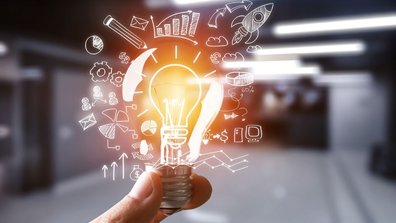 Eine Hand hält eine hell erleuchtete Glühbirne. Ringsherum schweben viele Symbole wie Diagramme und Computer.